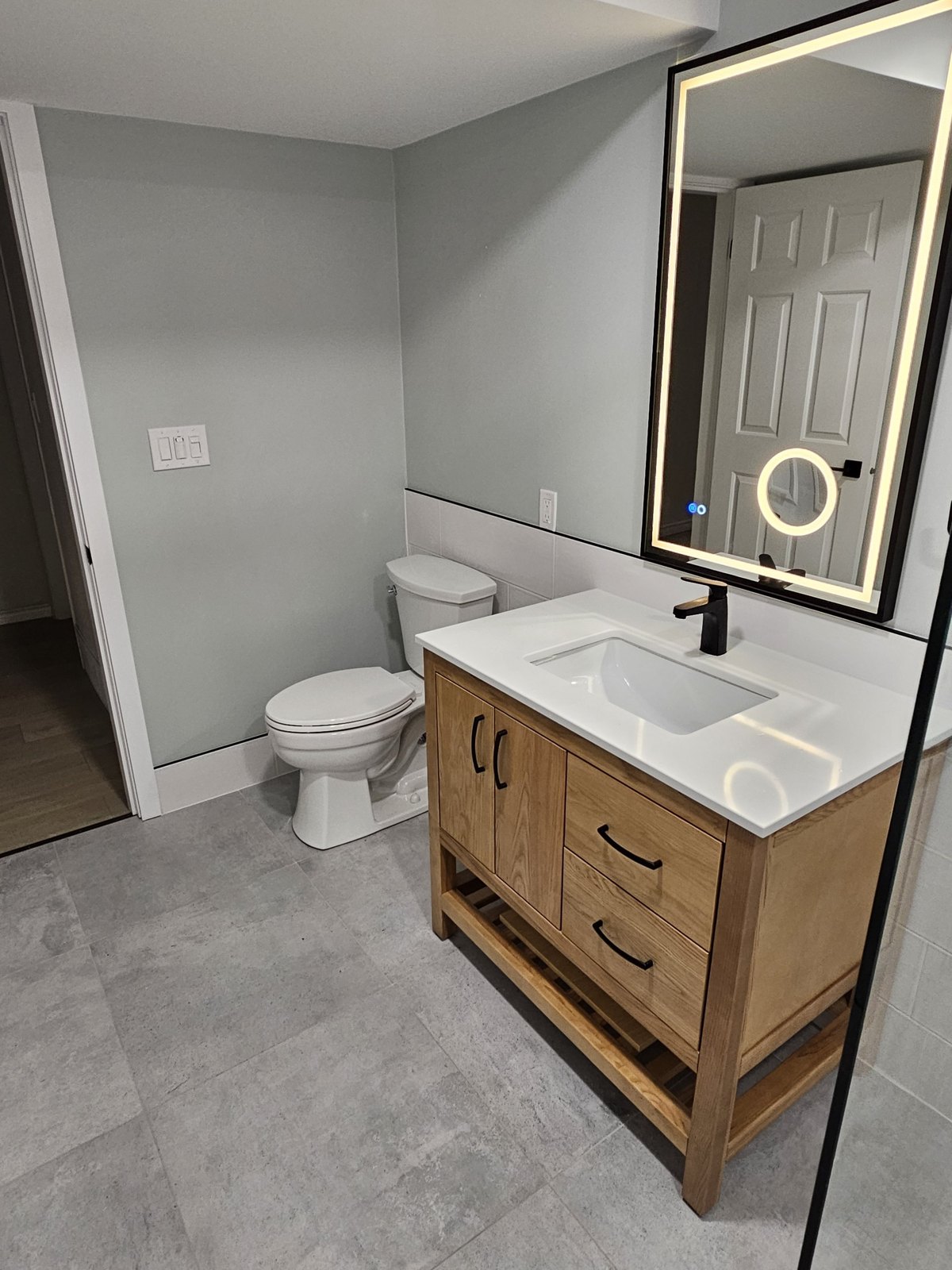 Bathroom with wood vanity, illuminated mirror and black faucet