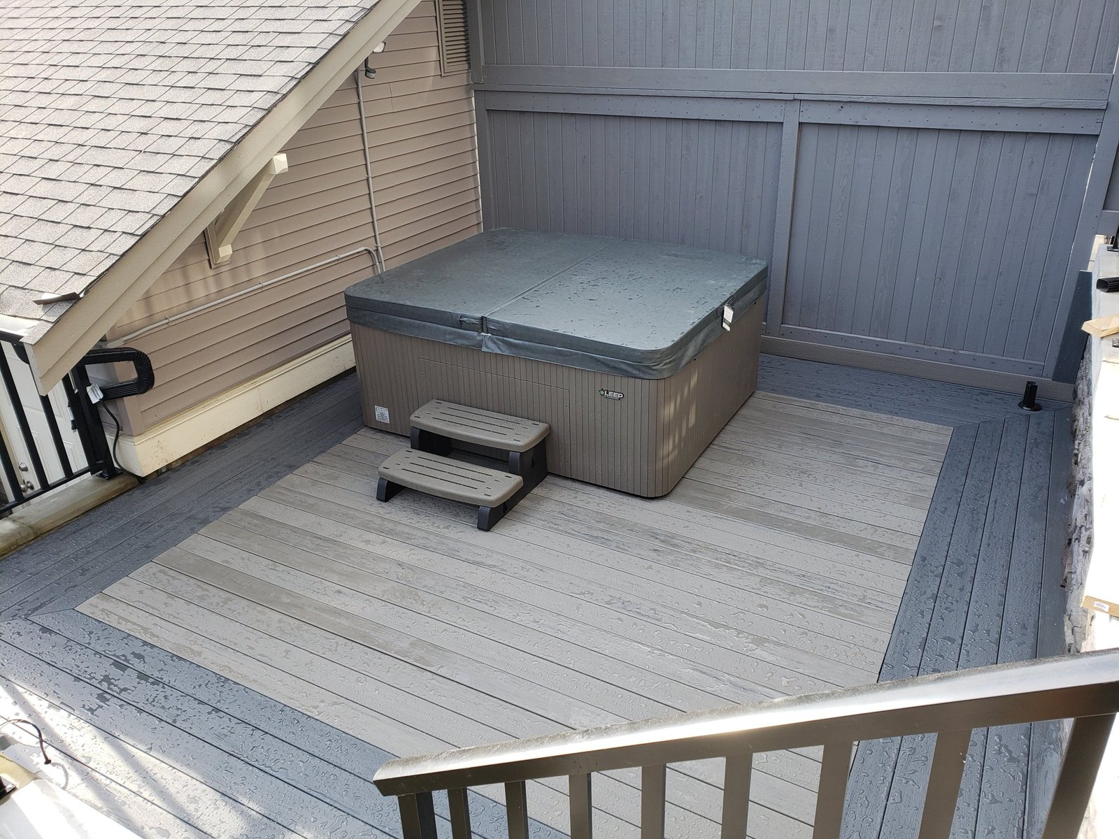 Grey deck surrounding a hot tub with privacy screening