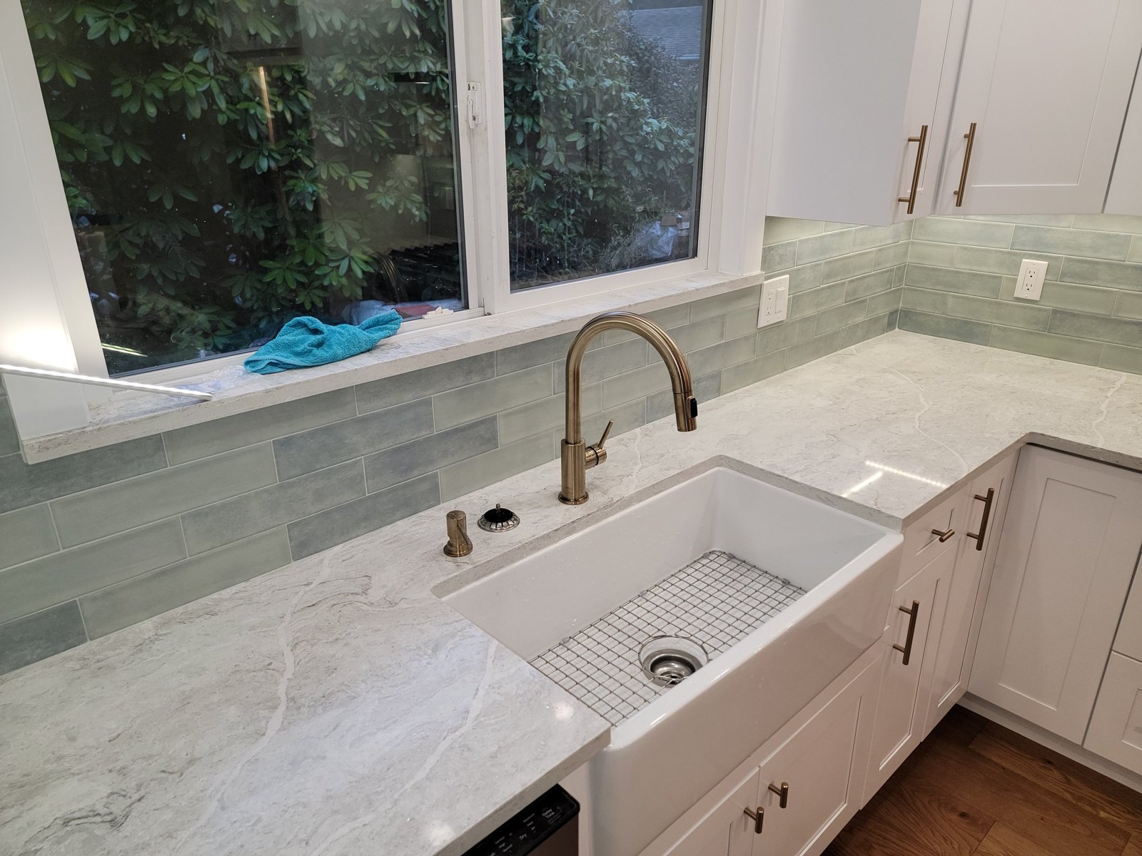 White kitchen sink, pale green tile backsplash and brass faucet