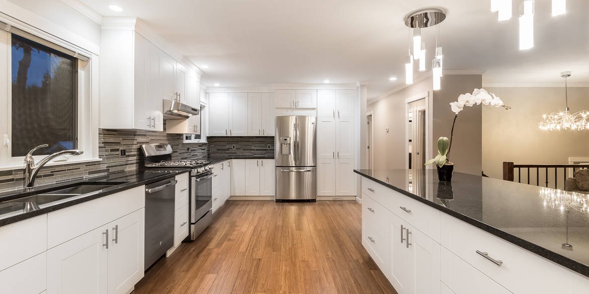 White kitchen with a long island, dark countertops and wood flooring